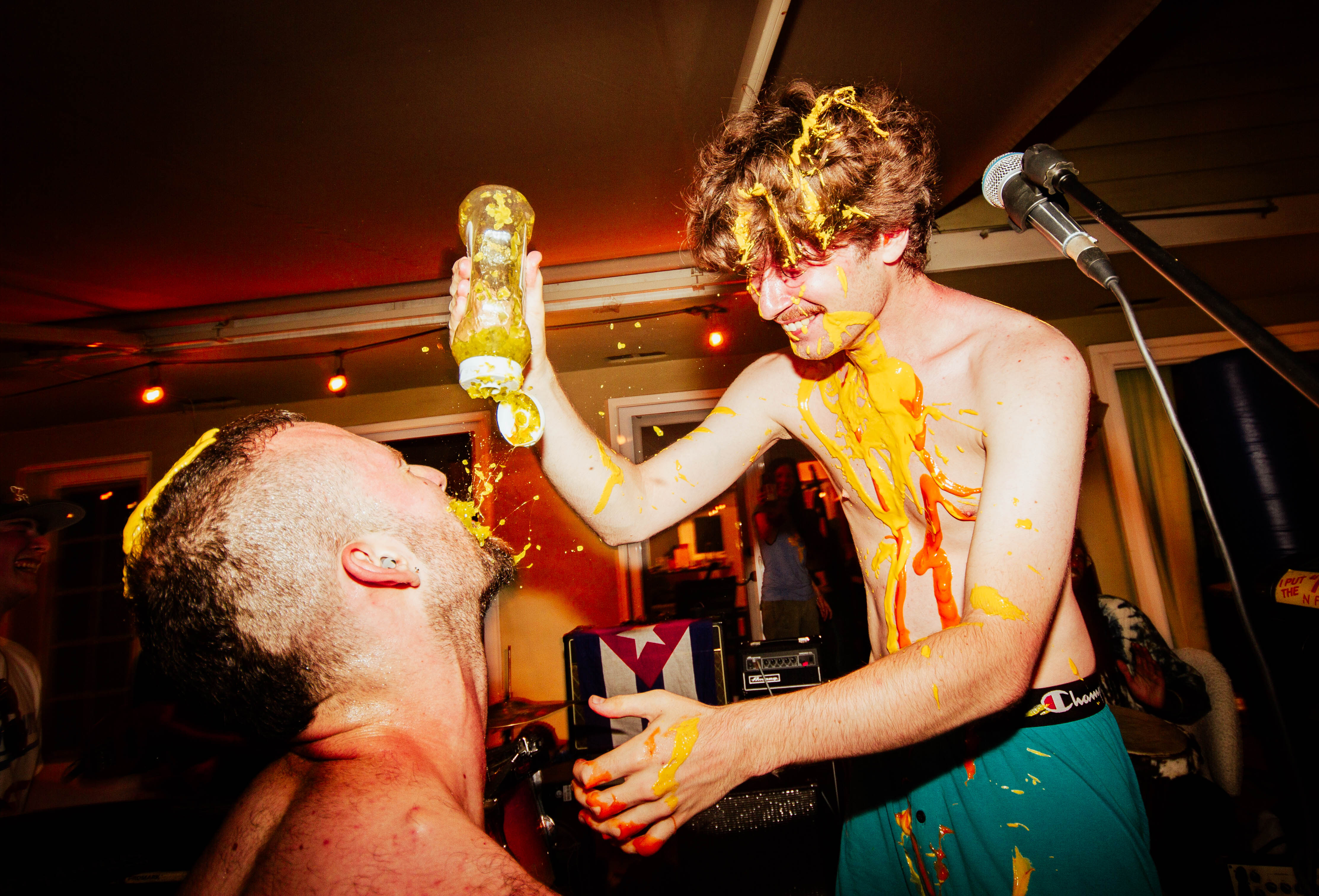 Cragen and Paolo McLeod Pesce, who plays drums and freestyle raps for Persona non grata, stand on stage, covering each other in condiments. The group often surprises the audience at shows with the unexpected. (Courtesy of Arturo Molina)
