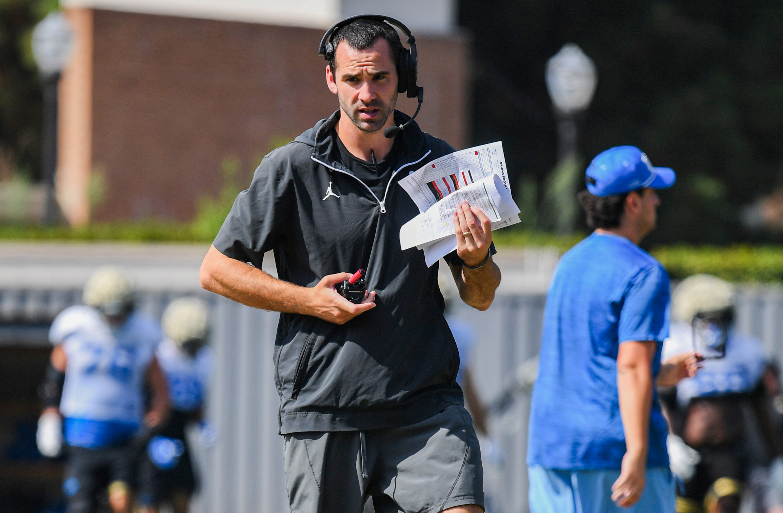 Offensive coordinator Dean Kennedy wears his headset as he calls plays on the field during practice Wednesday. (Kai Dizon/Assistant Photo editor)
