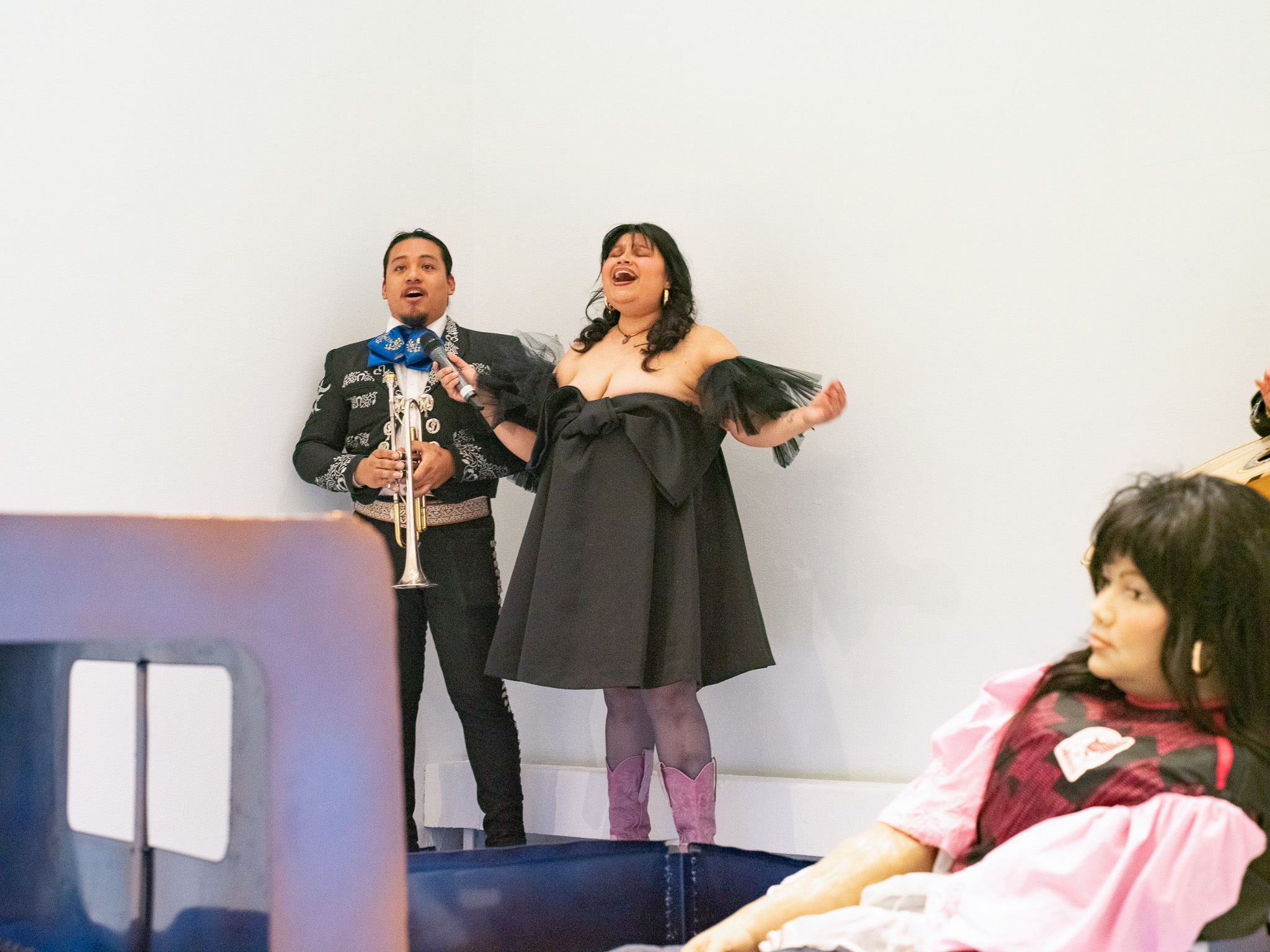 Barrios stands in a black dress and pink boots alongside a man holding a trumpet. The artist says UCLA provided her with the freedom to make whatever pieces she wished, creating opportunities to explore multiple art disciplines. (Courtesy of Pat Garcia and Davion Alston)