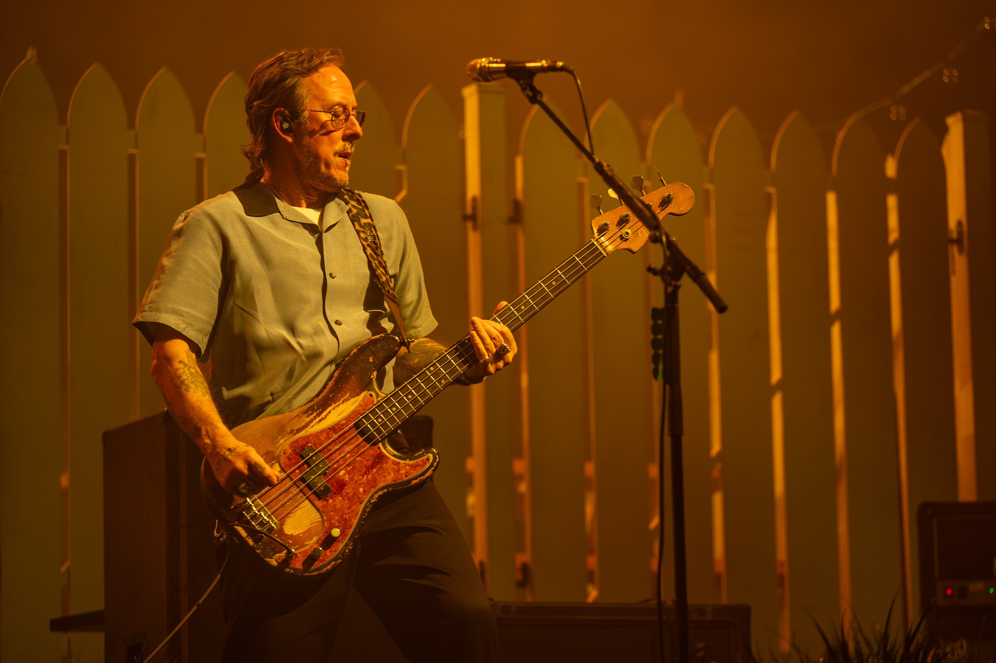 Weezer bassist stands against a white picket fence backdrop. The stripped-down songs of the night slowed the show and allowed attendees to sway in their seats and admire acoustic versions of popular songs. (Selin Filiz/Daily Bruin senior staff)