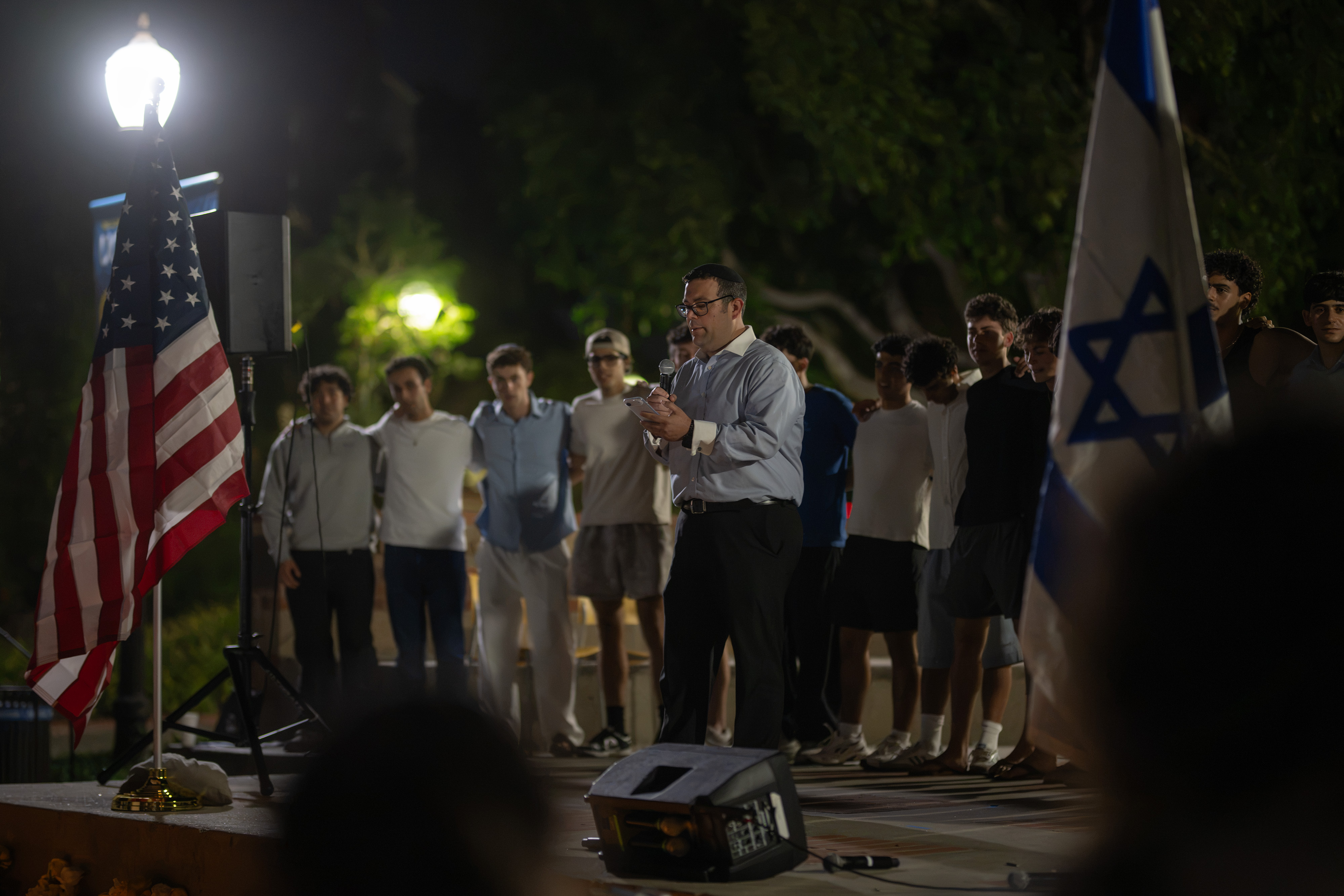 Speakers stood on McClure Stage, which was surrounded by candles and yellow and pink roses, Wednesday night during the vigil in Bruin Plaza. (Andrew Ramiro Diaz/Photo editor)