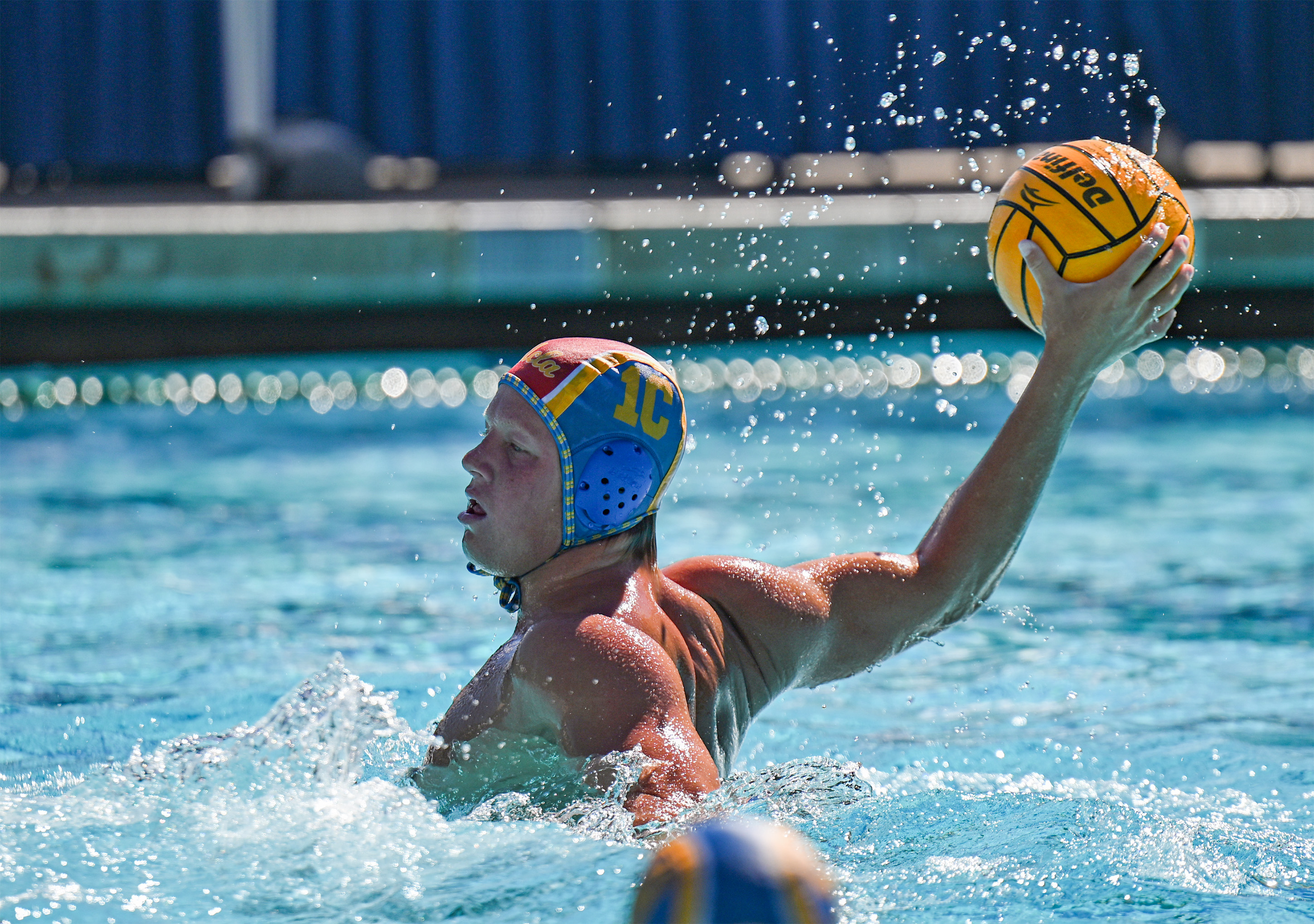 Junior attacker Ryder Dodd holds the ball above the water while donning the 1C cap. Dodd led the Bruins with five goals in Sunday's win over Cal. (William Gauvin/Daily Bruin staff)